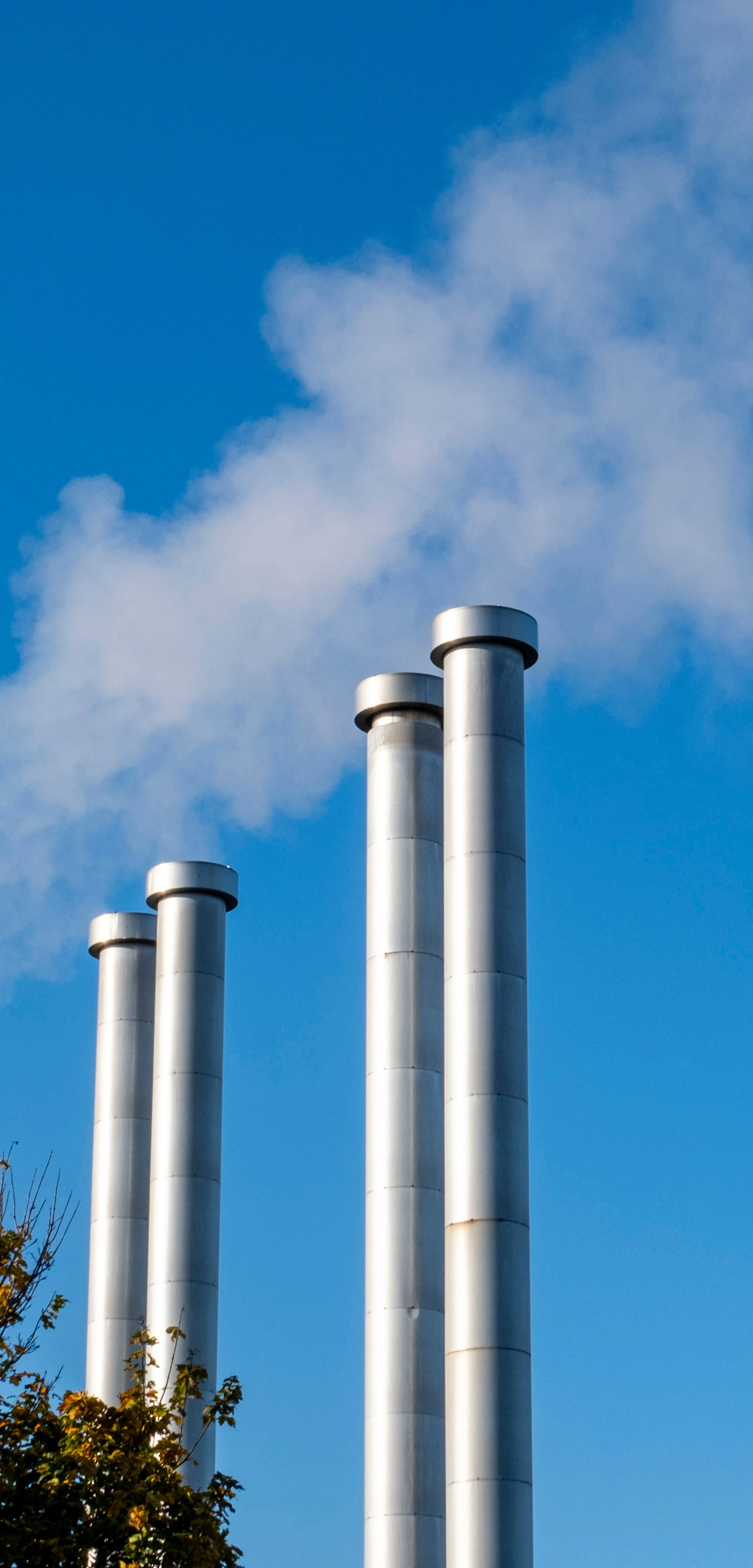 Vier hohe Industrieschornsteine stoßen weißen Rauch in den blauen Himmel