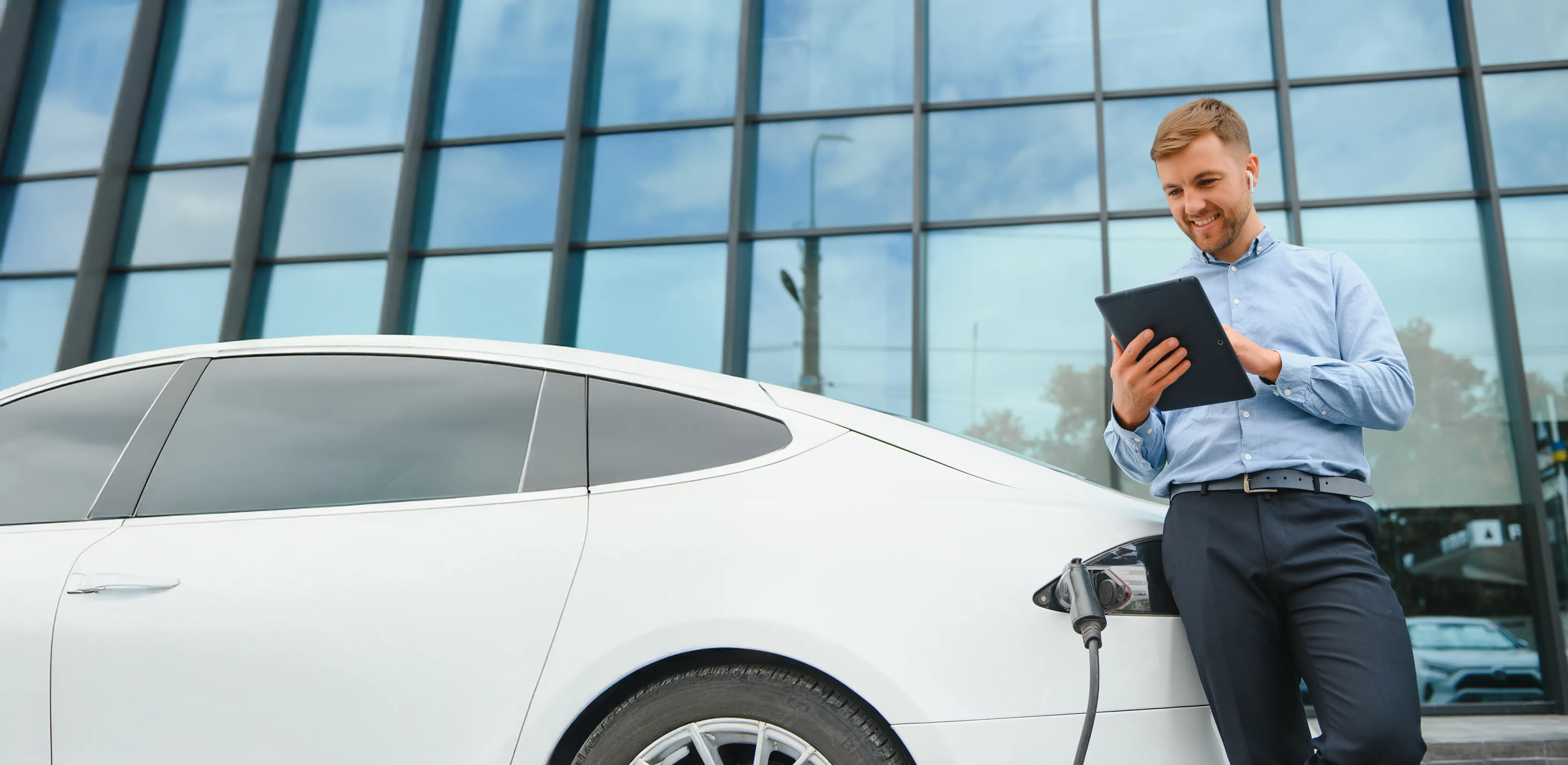 Mann lehnt an einem Elektroauto, das lädt, und schaut auf ein Tablet