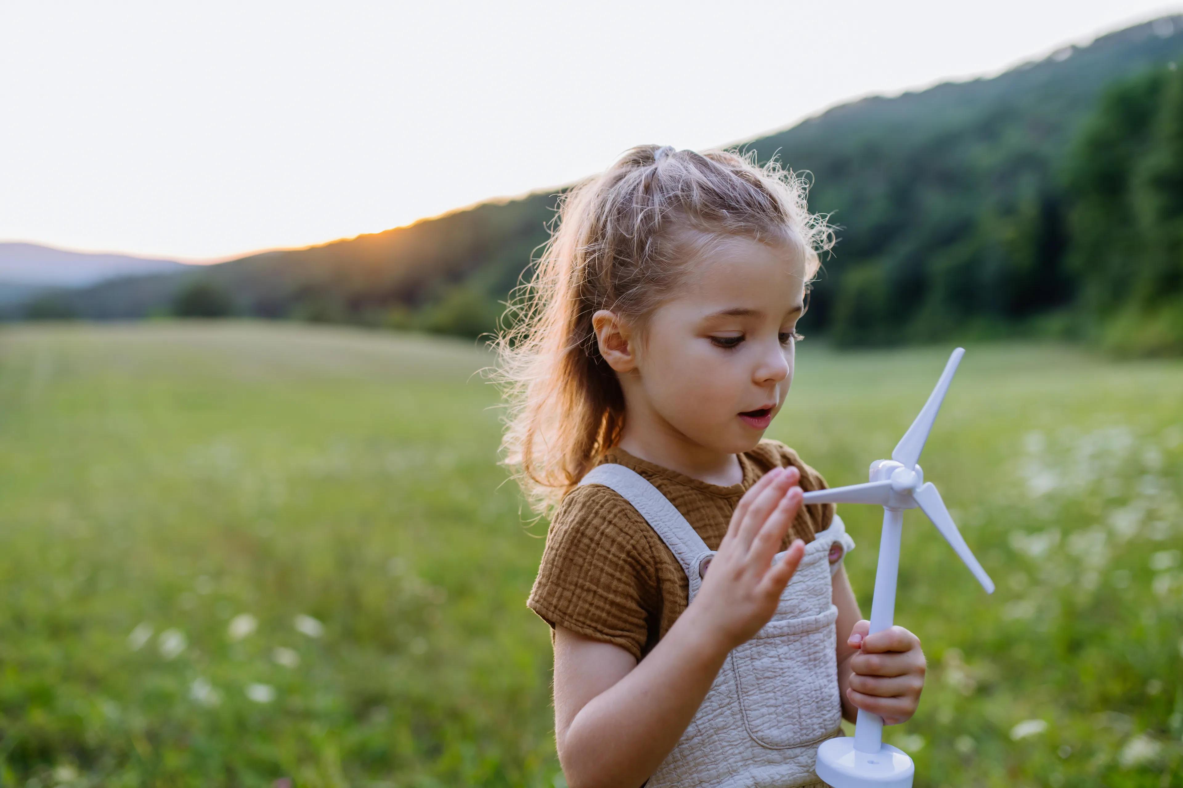 Kind steht mit Windradmodell auf einer Wiese