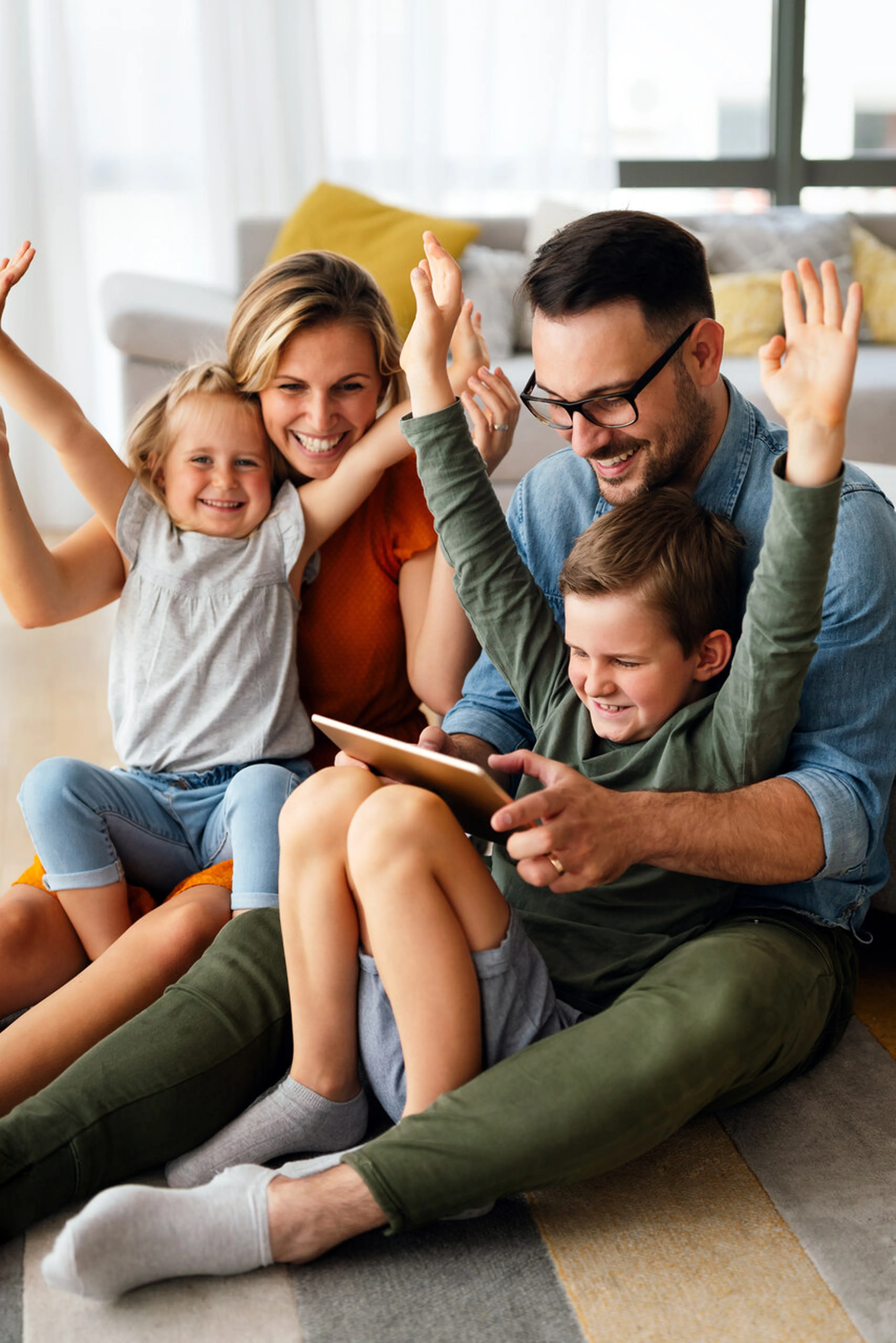 Familie sitzt auf dem Boden mit Tablet und jubelt mit Armen in der Luft